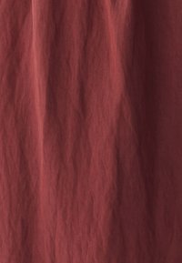 Roostes värvi kangas, millel on tekstureeritud ja kortsuline pind. Materjal tundub pehme ja kerge, sobides hästi rippumiseks või kihitamiseks.