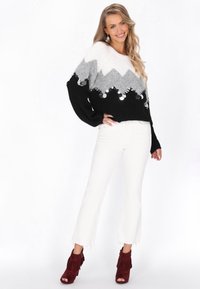 Fekete, fehér és szürke pulóver zig-zag mintával, ezüst paillettes díszítéssel. Fehér harangszárú nadrág és piros frufru bokacsizma teszi teljessé a megjelenést.