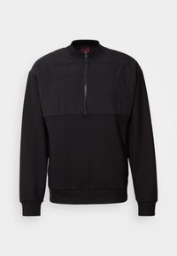 Schwarzer Herrenpullover mit gestepptem Oberbrustpaneel und Halbreißverschluss vorne, gerippten Bündchen und Saum sowie Stehkragen mit rotem "HUGO"-Etikett innen.