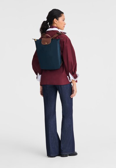 Navy blue backpack in durable fabric with a brown leather top handle and accents, featuring a medium rectangular shape and adjustable straps.