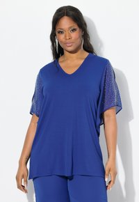 Top a V scollato e maniche corte in tessuto blu profondo con maniche in rete trasparente. Maniche impreziosite da piccole paillettes per un tocco in più.