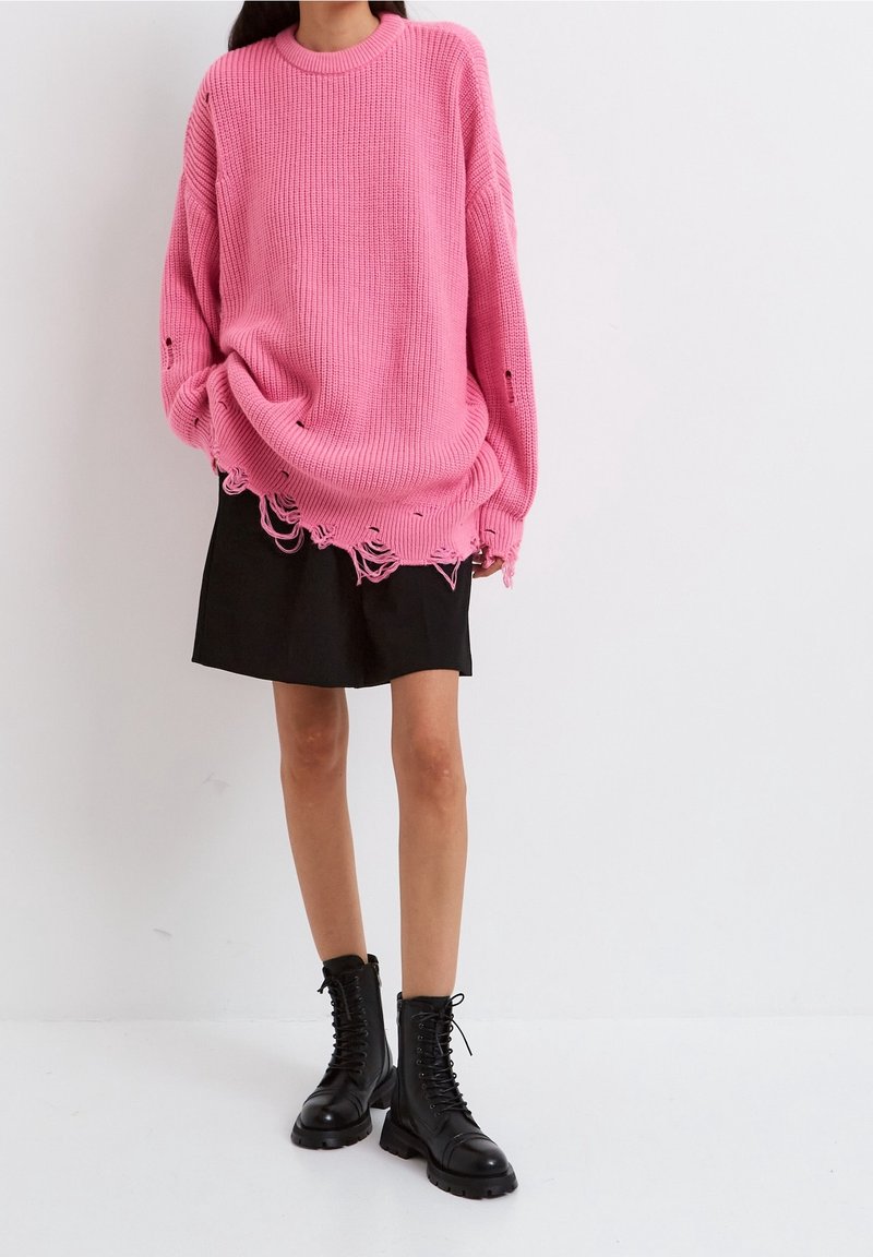 Lyserød strikket sweater med ribbet tekstur, oversized pasform, slidte kanter, parret med en sort mini skirt og sorte snørebånds combat boots.