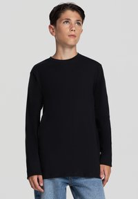 Czarna koszula z długim rękawem i okrągłym dekoltem, wykonana z miękkiego materiału. Posiada luźny krój i zestawiona jest z jasnoniebieskimi dżinsami.