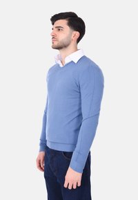 Maglione azzurro chiaro a V realizzato in morbido tessuto con maniche lunghe e polsini a costine. Indossato sopra una camicia bianca con colletto. Vestibilità casual.