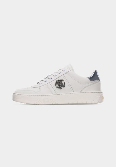 Λευκό sneaker χαμηλού τύπου με κορδόνια μπροστά, μαύρο λογότυπο στο πλάι και μαύρη λεπτομέρεια στο πίσω μέρος του γιακά, πάνω σε απλό ανοιχτό φόντο.