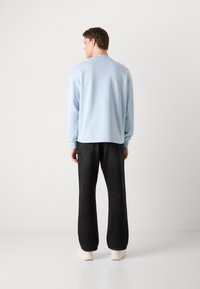 Felpa azzurra chiara con collo a giro e maniche lunghe, abbinata a jeans neri a gamba larga e scarpe beige, vista da dietro.