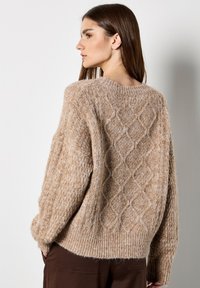 Maglione beige lavorato a maglia con un motivo a rombi texturizzato sul retro, orlo e polsini a coste, realizzato in morbido materiale peloso.