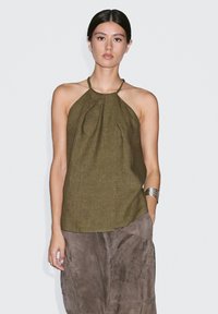 Olivově zelený halter top z lehkého materiálu s plisovaným předním dílem a odhaleným zadním dílem. V kombinaci s hnědou sukní z semiše a stříbrným náramkem.