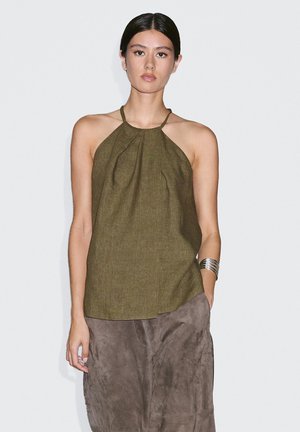 Haut halter vert olive en tissu léger avec un devant plissé et un dos ouvert. Assorti à une jupe en daim marron et à un bracelet en argent.