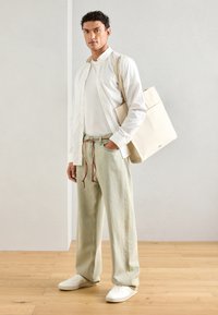 White button-up shirt over a fitted white t-shirt, paired with light green wide-leg pants and white sneakers. A beige tote bag is slung over one shoulder.
