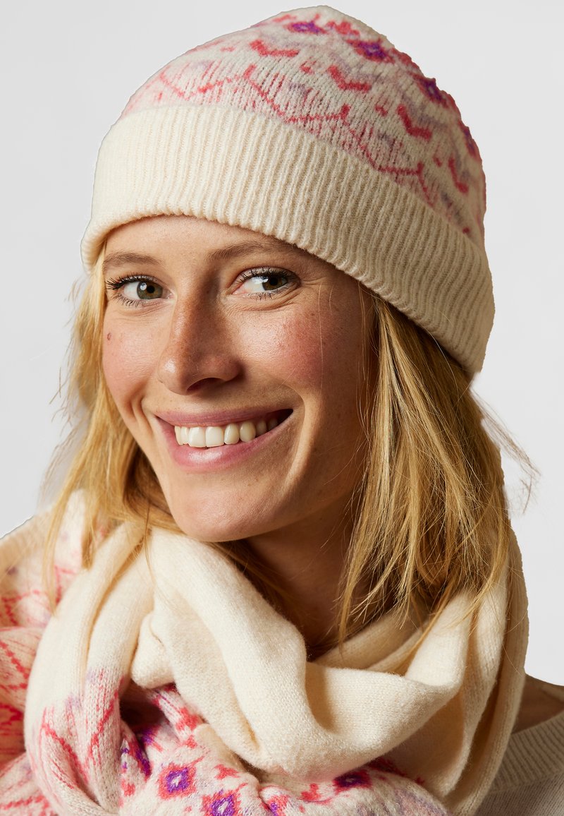 Bonnet en tricot crème avec des motifs rose et violet, associé à une écharpe crème, présentant une texture douce et une coupe décontractée.