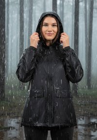 Giacca impermeabile nera con cappuccio, chiusura con zip, polsini elasticizzati e due tasche frontali, indossata da un modello sotto la pioggia.