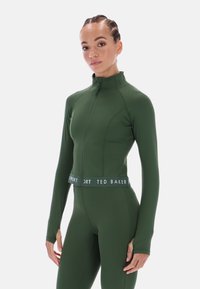 Zöld sportos cipzáras dzseki hosszú ujjakkal, félmagas nyakkal, texturált anyagból, és a deréknál "TED BAKER" feliratos kontrasztos szegéllyel.