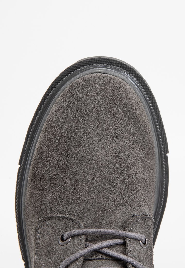 Grauer Wildlederschuh mit runder Zehenform, minimaler Schnürung, strukturiertem Obermaterial und kontrastierender schwarzer Gummisohle. Das Design ist elegant und modern.