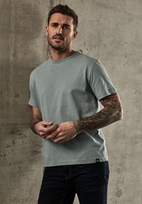 Světle modré bavlněné tričko s kulatým výstřihem, krátkými rukávy a tkanou štítkem na dolním lemu, v kombinaci s tmavými džínovými kalhotami.