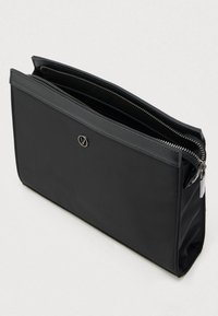 Musta suorakaiteen muotoinen pussi, jossa on vetoketjusuljin ja pieni pyöreä logo, esitetty hieman avoimena vaalealla yksinkertaisella taustalla.