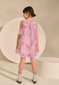Vestido rosa sin mangas con adornos florales en 3D y lentejuelas, combinado con botas de tobillo plateadas. Tela suave con un dise�ño fluido.