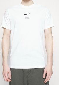 Vit bomull t-shirt med korta ärmar och rundad halsringning. Svart Nike-logotyp och text tryckt på bröstet. Enkelt mönster, normal passform.