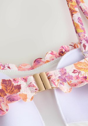 Weißer BH mit floralen gepunkteten Trägern und gewelltem Rand, verschlossen mit einem goldfarbenen Verschluss. Strukturierter Stoff mit sanften floralen Mustern.