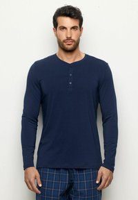 Námořnická dlouhá košile henley s kulatým výstřihem, zapínáním na knoflíky a měkkou tkaninou. Nosit s kostkovanými pyžamovými kalhotami.