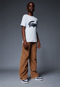 T-shirt en coton bleu clair avec un graphique de crocodile noir, associé à un pantalon en velours côtelé large marron et des baskets bleu marine et blanches.