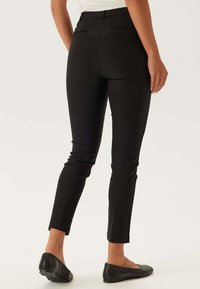 Pantaloni neri attillati con una texture liscia, vita media e tasche posteriori. Il design si restringe verso la caviglia, abbinati a scarpe basse.