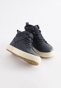 Paire de baskets montantes noires avec semelles épaisses beige et col rembourré, inclinées pour montrer les vues latérale et supérieure sur fond blanc.