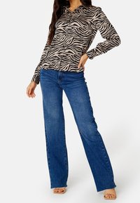 Chemise à manches longues à boutons avec imprimé zèbre beige et noir, associée à un jean large bleu. La chemise présente un col classique et une coupe ajustée.