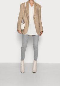 Beiger oversized Blazer, darunter ein weißes Hemd, graue enge Jeans und helle Stiefeletten. Kleine helle Tasche mit Kettenriemen.