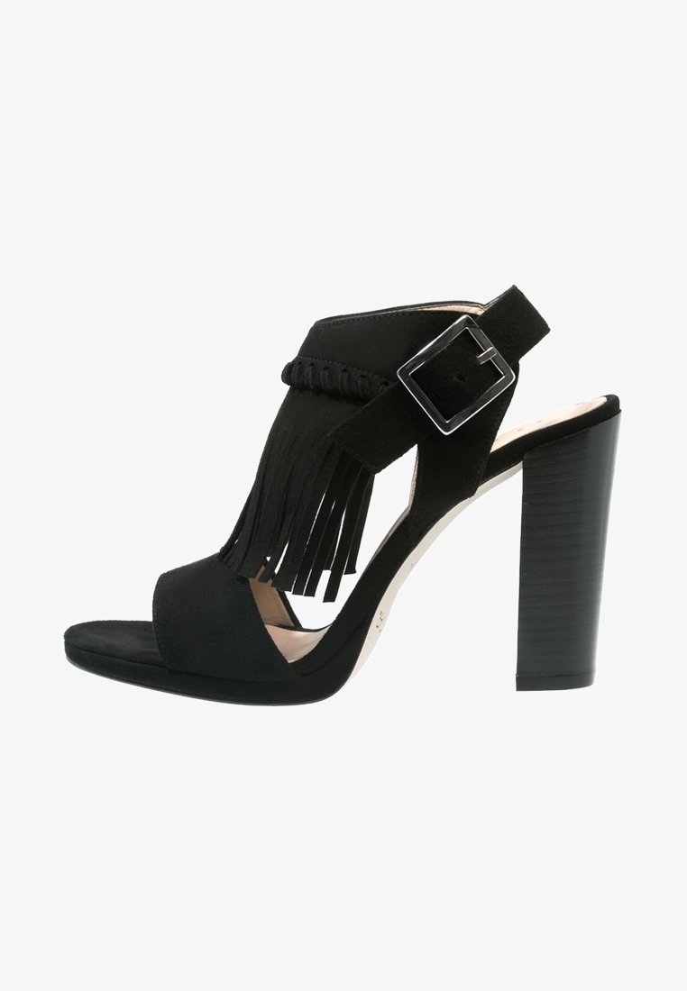 Sandale noire à talons hauts avec un bout ouvert, en suède, détail frangé et une sangle à boucle réglable. Elle présente un talon empilé.