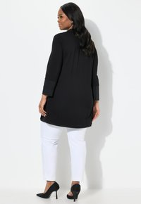 Schwarzes Tunika-Oberteil mit Dreiviertelärmeln, kombiniert mit weißen, schmal geschnittenen Hosen. Das Ensemble verfügt über eine glatte Textur und eine lockere Silhouette.