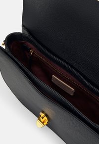 Schwarze Lederhandtasche mit strukturiertem Oberflächen, goldfarbenem Verschluss und burgunderfarbenem Innenraum, der eine Reißverschlusstasche und ein Markenlabel beinhaltet.