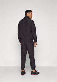 Schwarzer Sportanzug mit Zip-Jacke und elastischen Bündchen. Ausgestattet mit einer glatten Textur und ergänzt durch schwarze und rote Sneakers.