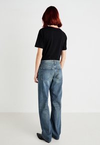 Svart kortermet t-skjorte kombinert med lyseblå, løstsittende jeans med en falmet tekstur og standard baklommer.