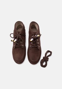 Ζευγάρι καφέ μοκασίνια σουέτ με κορδόνια διακοσμημένα με χάντρες και διπλωμένη λεπτομέρεια με φούντες, συνοδευόμενα από ένα επιπλέον ζευγάρι καφέ κορδόνια παπουτσιών.