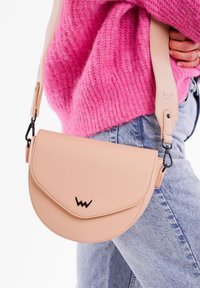Růžovo-peachová kožená kabelka přes rameno s zakřiveným klopou, černým logem a nastavitelným popruhem upevněným kovovými sponami. Texturovaná pro lepší uchopení.