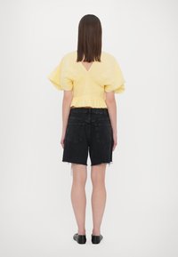 Top giallo a maniche puff con texture arricciata e schiena a V, abbinato a pantaloni corti in denim neri a vita alta con orli sfilacciati. Ballerine nere.