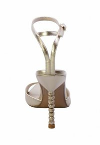 Sandali beige con tacco alto, caratterizzati da cinturini metallici e un tacco decorato con strass. Design aperto sul retro e sulla punta.