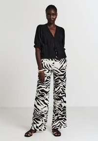 Blusa nera con maniche a sbuffo e dettagli con fiocco in vita, abbinata a pantaloni larghi con un audace motivo a zebra bianco e nero.