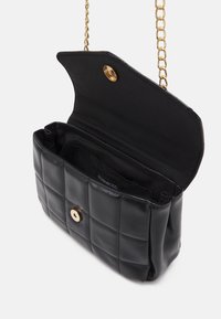 Bolso acolchado negro con herrajes dorados, que presenta una correa de cadena y un único compartimento con cierre magnético. Textura suave y lisa.