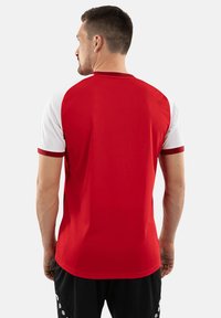 T-shirt de sport rouge avec des manches courtes blanches, un col rond et une bordure rouge contrastante sur les manches. Tissu lisse et léger.