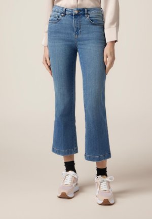 Vaqueros cortos de mezclilla azul claro con dobladillo acampanado, diseño de cinco bolsillos y detalles de costura. Combinados con zapatillas blancas y rosas.