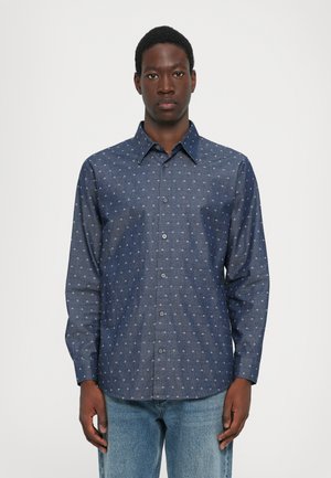 Mørk denimskjorte med knappelukking, lange ermer og et hvitt geometrisk mønster over det hele. Klassisk krage og rett nederkant.