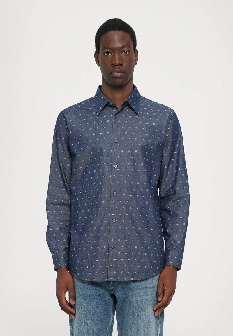Camisa de denim oscuro con un diseño de botones, mangas largas y un patrón geométrico blanco en todo su tejido. Cuello clásico y dobladillo recto.