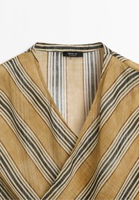 Overhemd met kraag met diagonale beige, zwarte en witte strepen en een zwart merklabel met de tekst Massimo Dutti Made in Morocco.