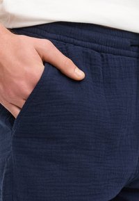 Navyblauwe broek van textuurstof met een relaxte pasvorm. Voorzien van zijzakken en een elastische tailleband voor comfort.