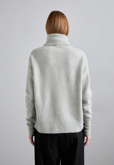 Maglione grigio chiaro di grande taglia con colletto a coste alto, maniche lunghe e tessuto morbido, abbinato a pantaloni neri.