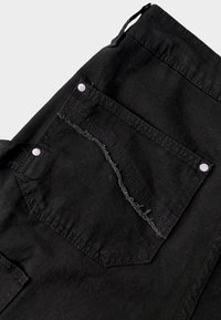 Zwarte denim broek met een rafelige zak en contrasterende stiksels, voorzien van twee drukknoopsluitingen. De stof heeft een gladde, gestructureerde oppervlakte.