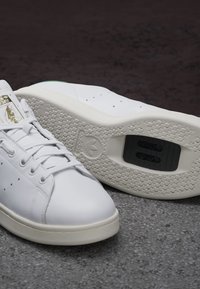 Białe skórzane sneakersy z perforowanymi detalami, sznurowanym zapięciem, teksturowaną gumową podeszwą i logo na języku.