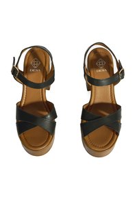 Schwarze Plateausandalen mit überkreuzten Lederriemen, verstellbarem Knöchelverschluss und braunem gepolstertem Fußbett. Holzähnliches Sohlendesign.
